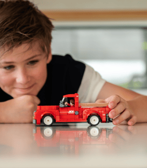 A young boy playing with a red NovaBrix Ace Hardware Vintage Truck