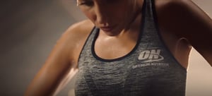 A close up of a woman exercising wearing a dark grey Optimum Nutrition singlet