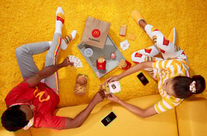 Two teenagers in McDonalds clothing eating their McDelivery Order on yellow carpet and furnature while playing cards
